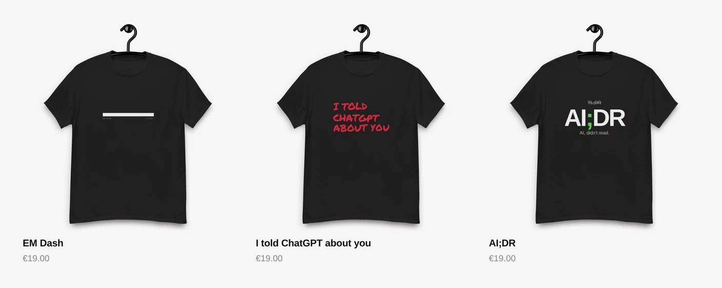 Three black T-shirts on hangers against a light grey background: EM Dash with a white bar, I told ChatGPT about you in red handwritten lettering, and AI;DR with a green semicolon. Each priced at 19 euro.